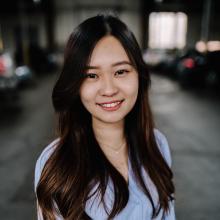 A woman in a blue blouse smiles in a parking garage.