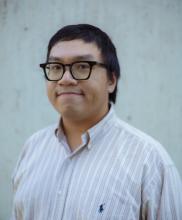 A person in a white shirt stands in front of a white background.