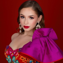 A person wears a red dress and stands in front of a red background.