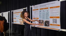 A person gestures towards a research poster at a conference.
