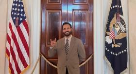 A person in a suit makes the Hook 'em hand sign between two American flags.