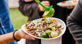 A person ladles some sauce over a plate of tacos.