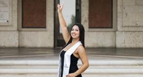 Leylah Attia poses in a white sash in front of a campus building.