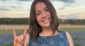 Hannah Justvig Vaughan poses with a Hook 'em hand sign in an outdoor headshot.