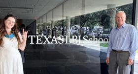 Emma and Jim Niewald pose in front of a glass window depicting the Texas LBJ School logo.