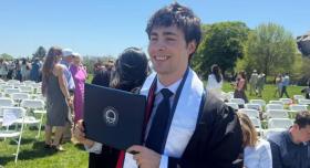 Eli Craddock poses with his diploma at an outdoor graduation ceremony.