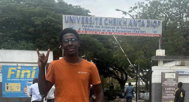 Devarier Smith wears an orange shirt and makes the hook 'em horns sign in front of the Universite Cheikh Anta Diop in Senegal.