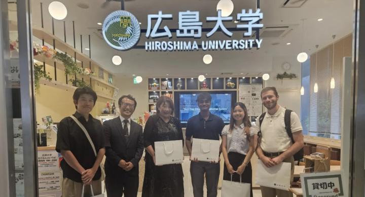 Five people wear business casual wear and stand holding white shopping bags in a cafe.