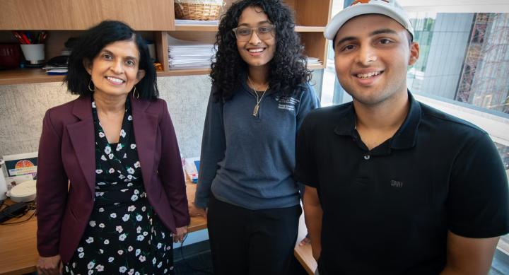Three people wear business casual clothes and stand in an office.