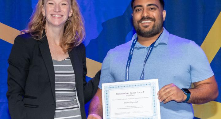 A man and woman stand in front of a blue background holding a certificate for the 2025 Student Poster Award.