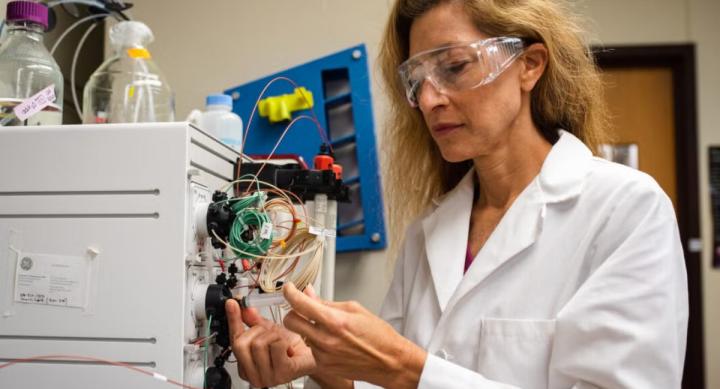 A researcher in a lab coat inserts a syringe into a machine.