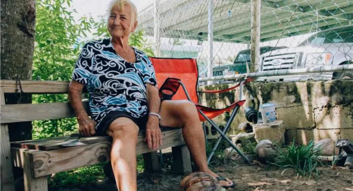 A person sits on a bench next to a fenced-in parking lot.