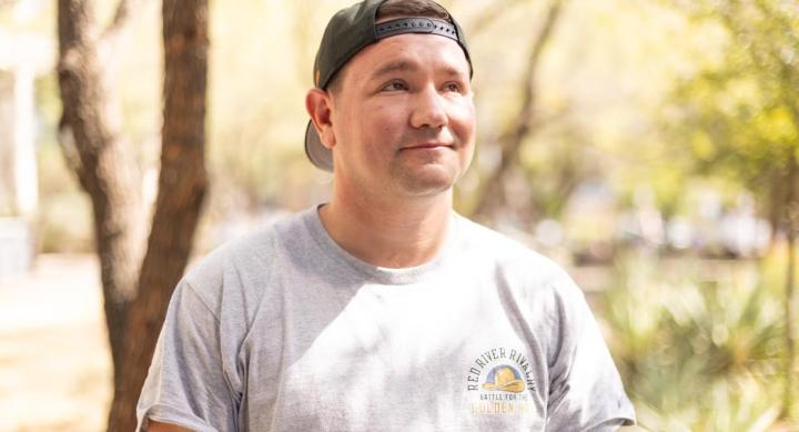 A person stands outdoors wearing a baseball cap.