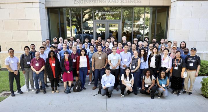 A large group of people wearing lanyards stands in front of the Oden Institute academic building.