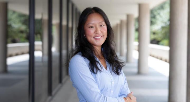 A person in a blue shirt stands outside a campus building.