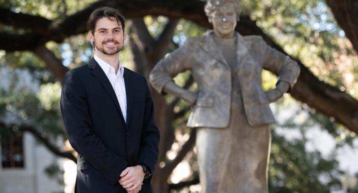 A person in a suit poses in front of the Barbara Jordan statue on the UT campus.