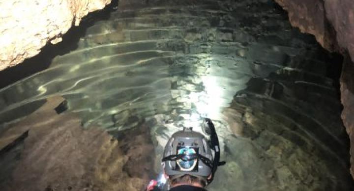 A person in a wetsuit squats inside of a cave.