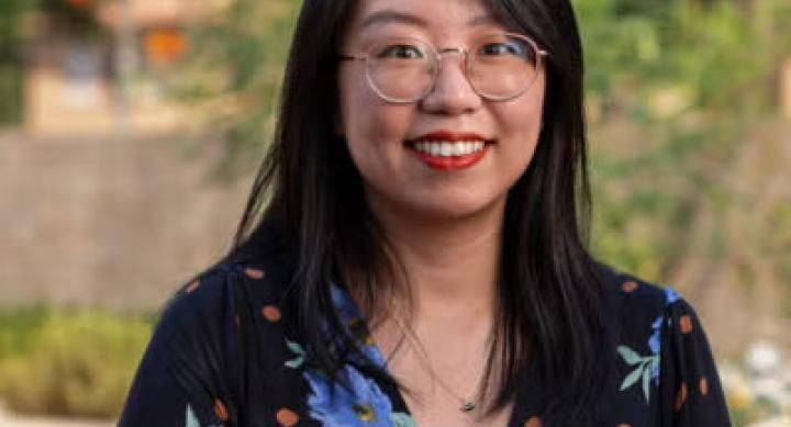 A person in a floral blouse and glasses poses for a headshot on campus.