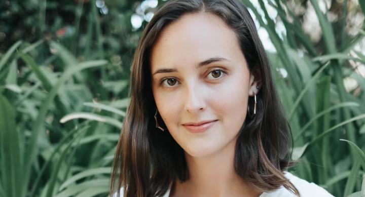 A person poses for a headshot in front of blades of tall grass.