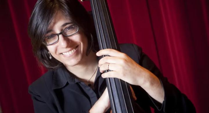 A person poses with a bass in front of a red curtain.